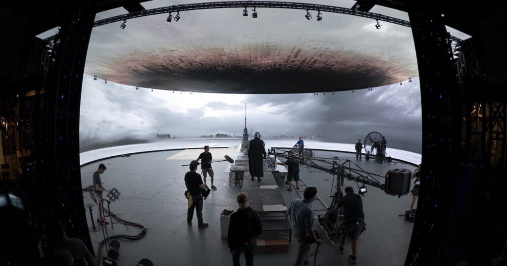 Behind-the-scenes image from the set of Disney's The Mandalorian. Mando and the crew filming in a soundstage surrounded by the giant digital screens of Lucasfilm's StageCraft system.
