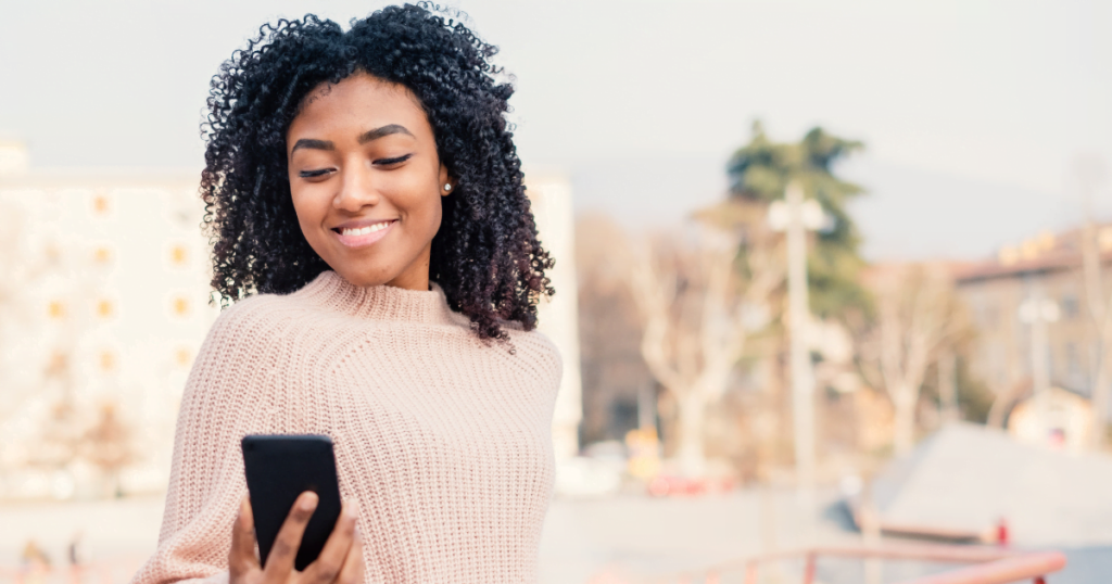 A Black woman smiling at her smartphone.