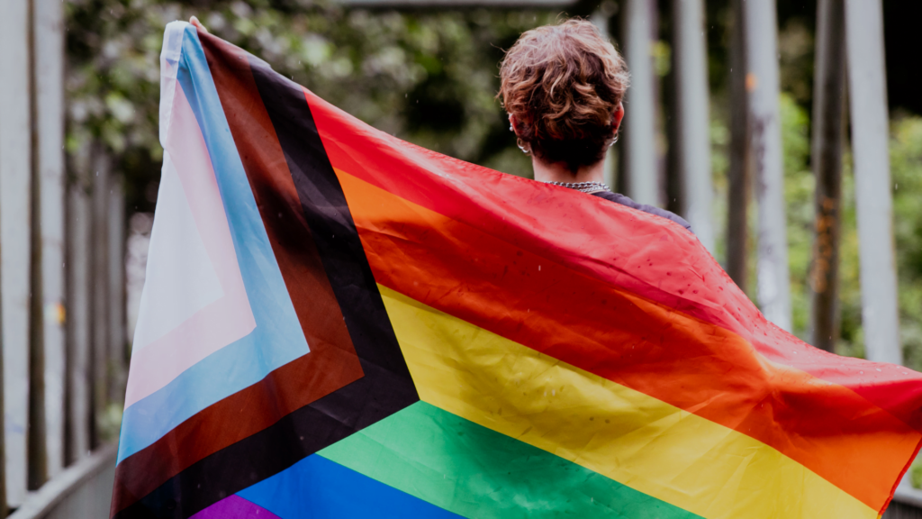 A person holding a bright rainbow flag, showcasing solidarity and celebration of 2SLGBTQ+ rights and diversity.