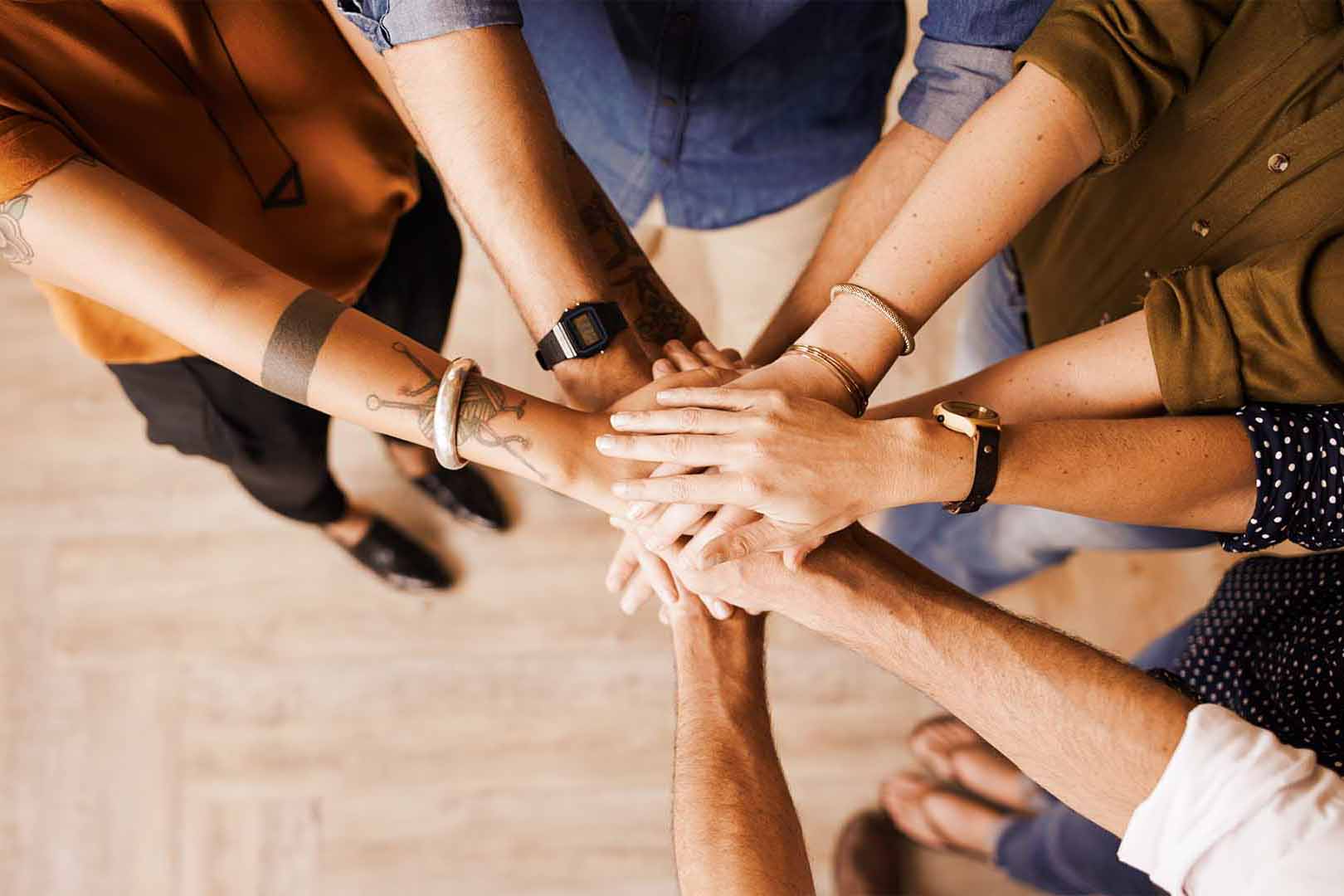 A group of people standing in a circle with their hands stacked on top of each other as a sign of teamwork.