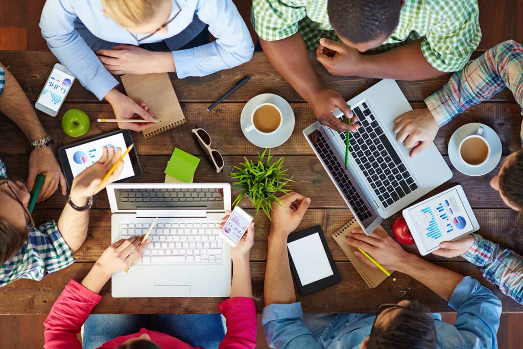 Colleagues collaborating at a shared table with laptops and coffee