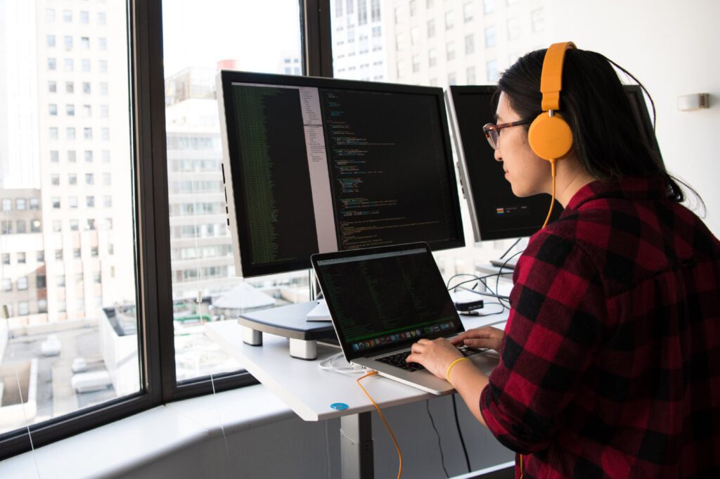 Developer with headphones coding at a standing desk by a city window